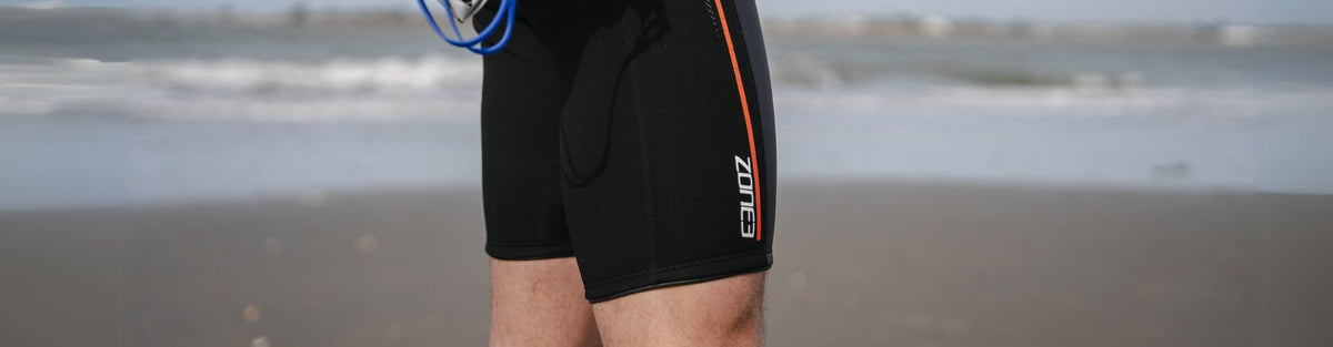 Een zwemmer op een strand in zwarte ZONE3 buoyancy shorts, zichtbaar vanaf het middel naar beneden.
