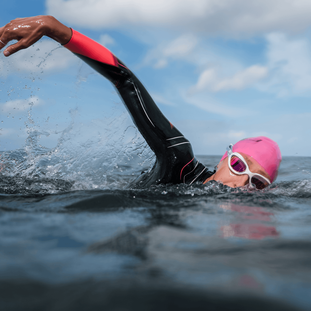 Arm van een zwemmer in een zwarte en roze wetsuitmouw spettert water tijdens het zwemmen.
