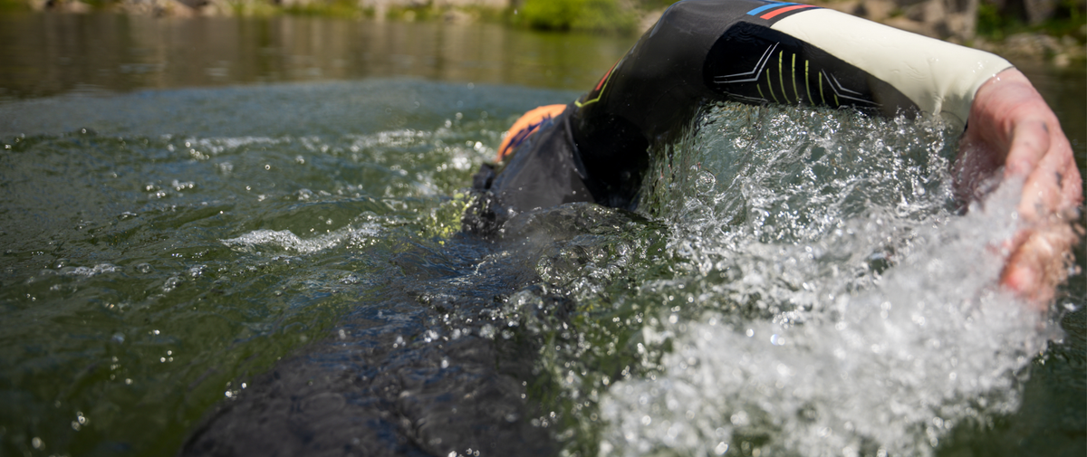 Person swimming in a ZONE3 Aspire wetsuit in open water. The person is in front-crawl with their head under the water and right hand emerging from the water to complete the stroke.
