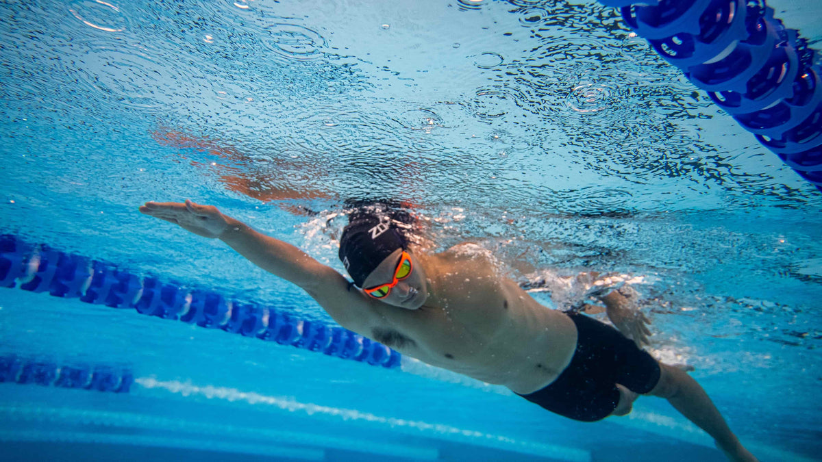 Athlete training in the pool wearing black zone3 swim cap and the navy neon orange attack swim goggles.