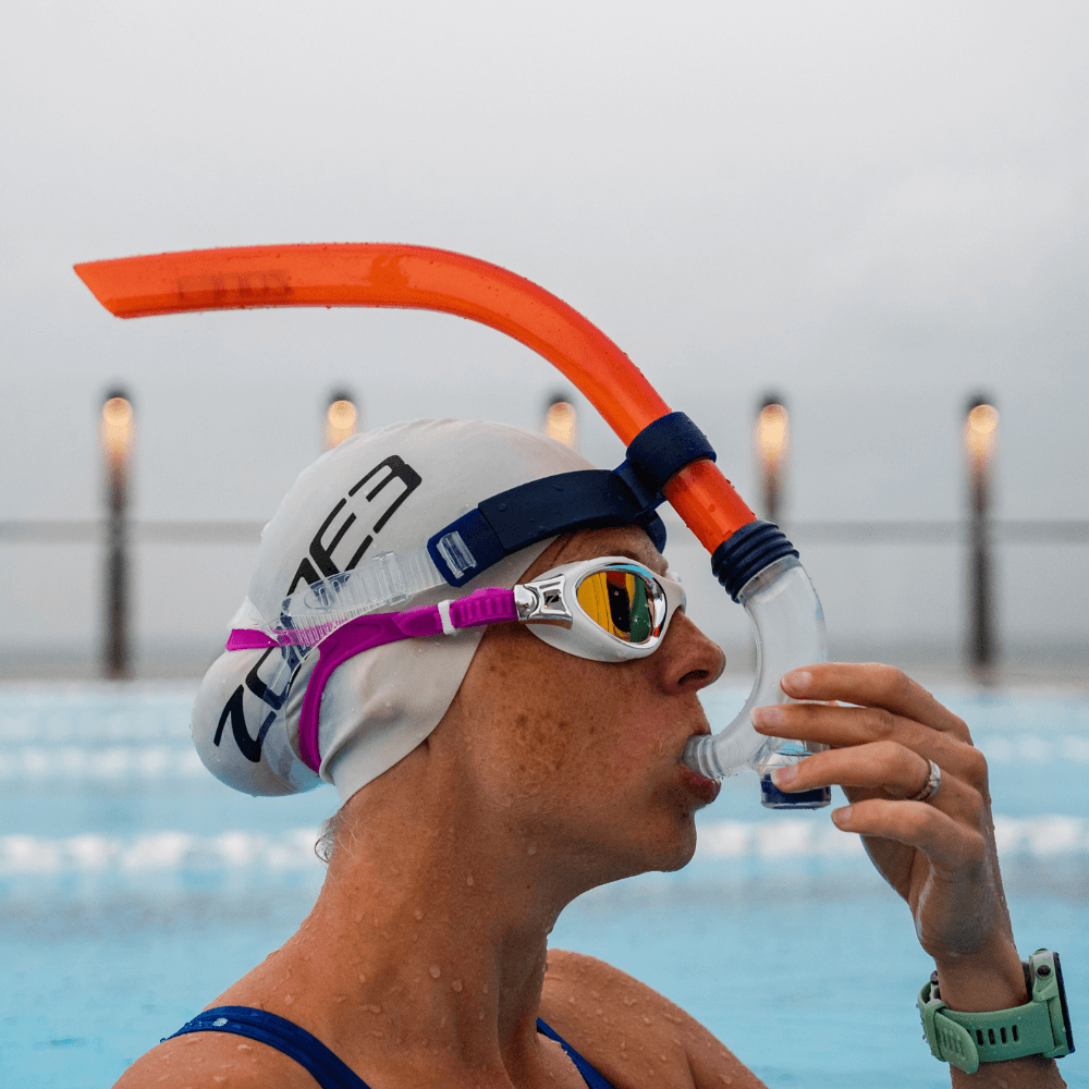 Swimmer wearing a white swim cap pink strap goggles and bright orange front facing snorkel during training in a pool