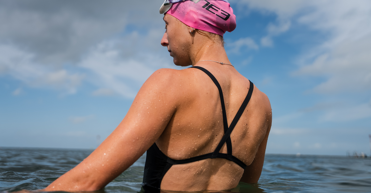 Person wearing a swim cap and black swimsuit in the water with a blue sky background