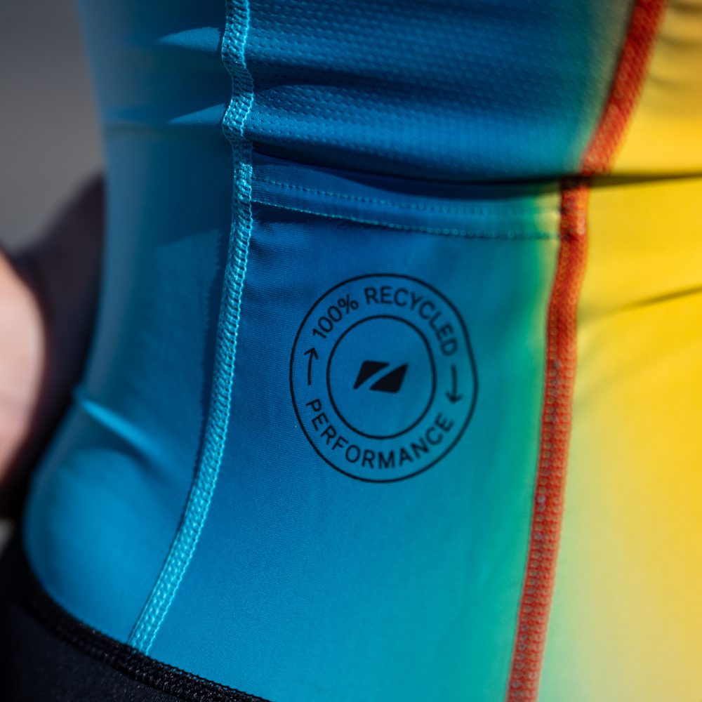 Close-up of the trisuit's rear side panel showing the text "100% Recycled Performance" printed on the light blue fabric.