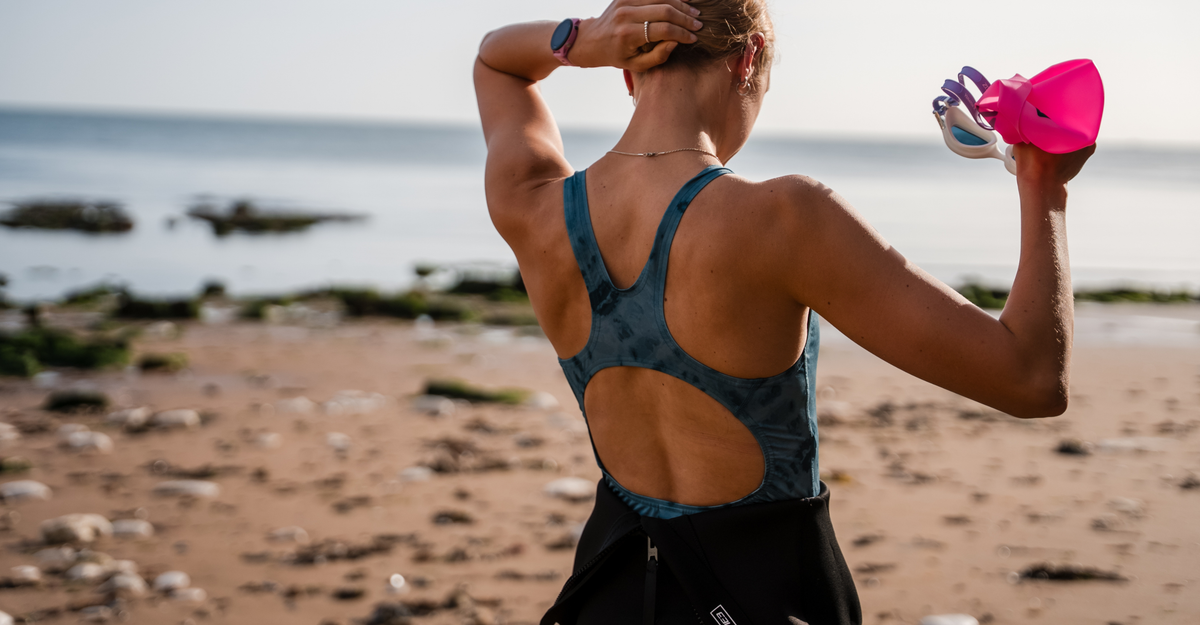 Person in teal tie-dye swimwear standing on a beach with ocean view