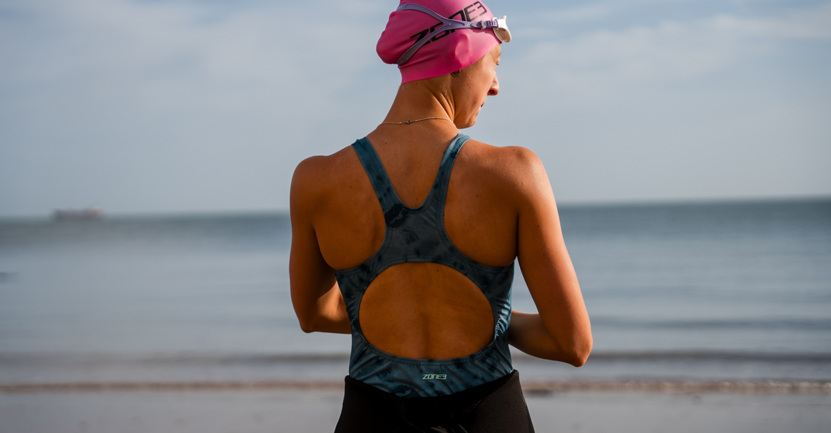 Person wearing a teal tie-dye swimsuit and swim cap on a beach