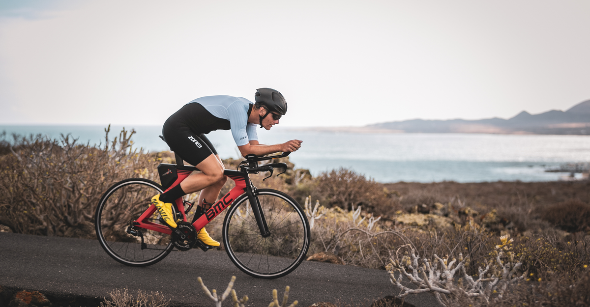 Person riding a bicycle in the lava trisuit on a trail with a scenic background