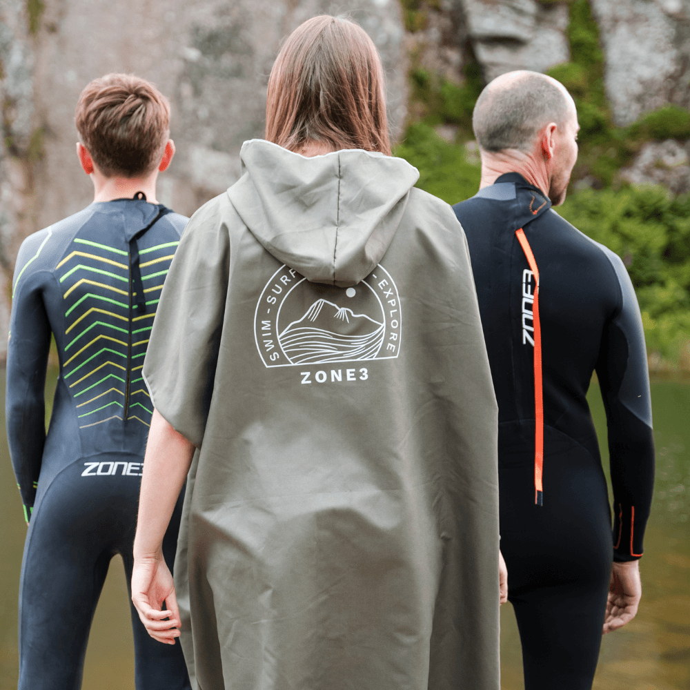 Three individuals wearing wetsuits and a Microfibre Changing Robe by Zone3, ideal for outdoor swimming and adventures.