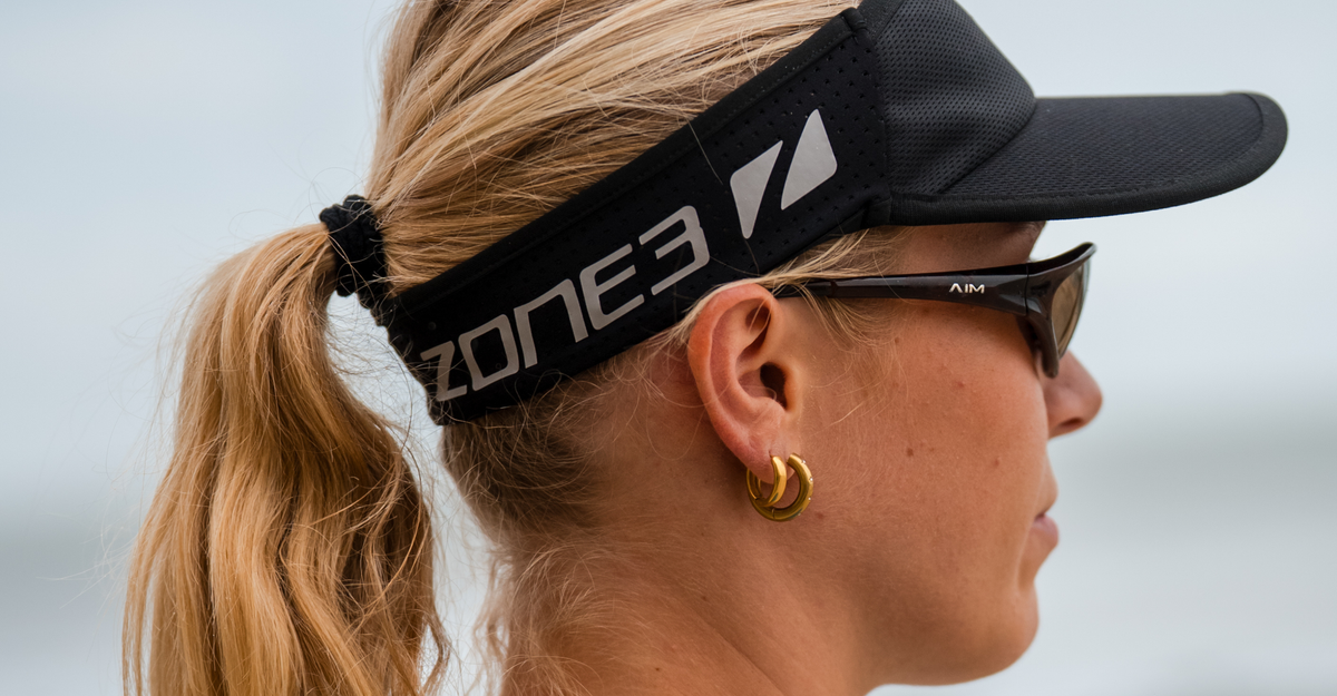 Woman wearing zone3 black running visor with a zone3 logo on a blurred background