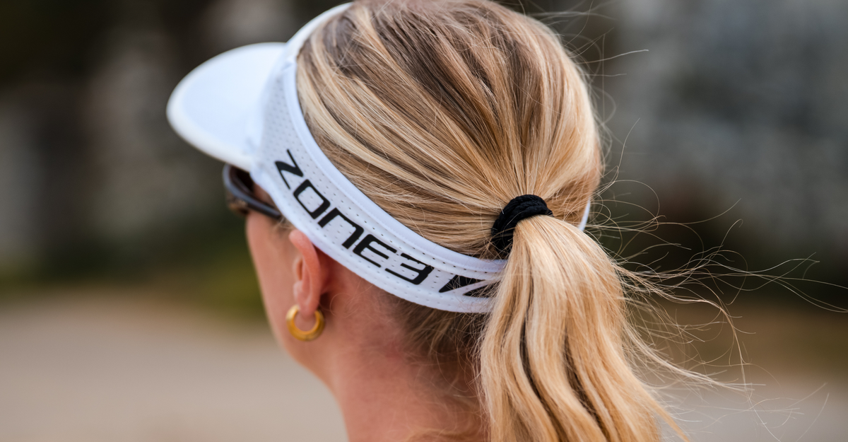 Woman wearing glasses and a zone3 white running visor with a zone3 logo on a blurred background