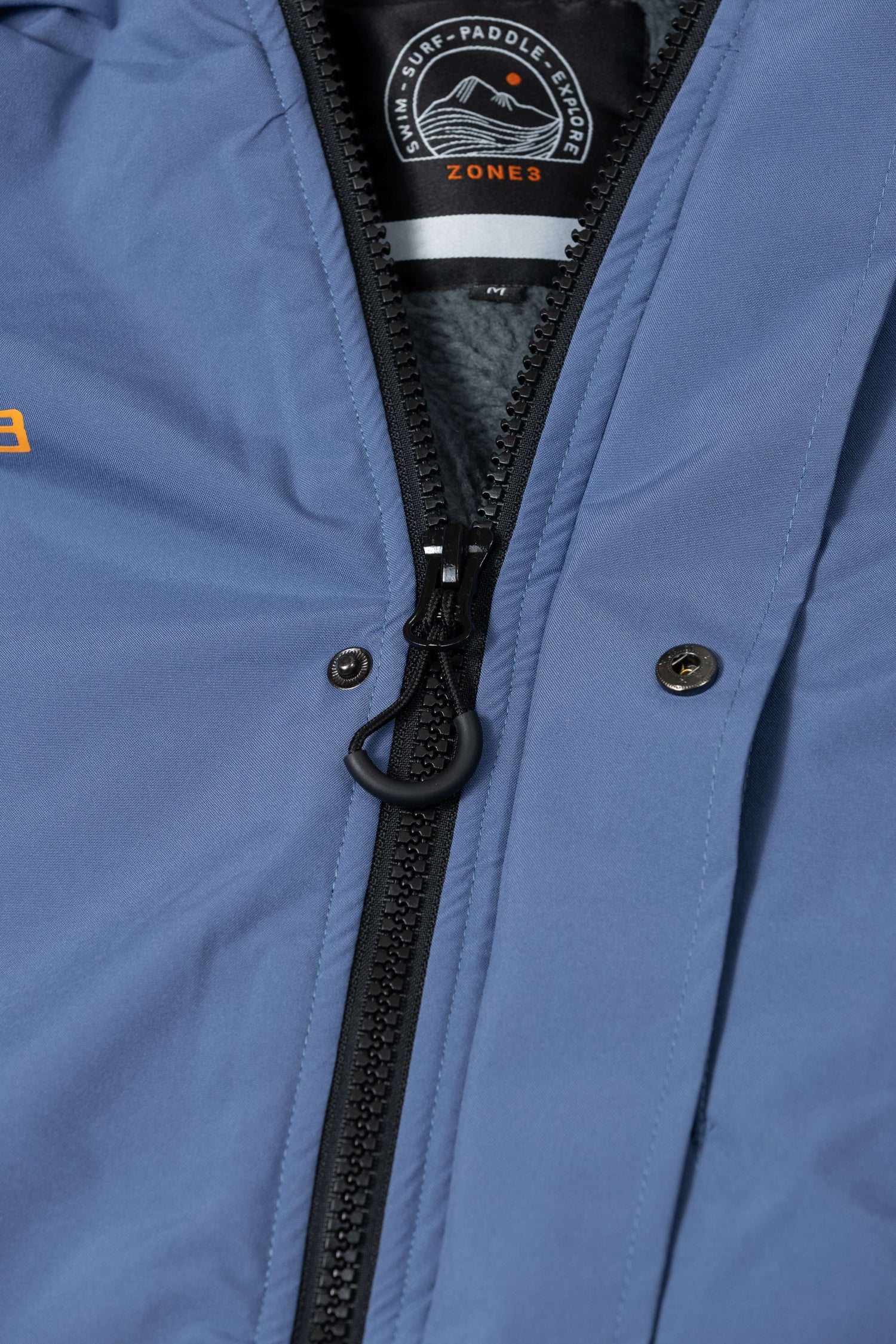Close-up of the robe's front zip, with visible branded pull tab and logo patch inside the collar.
