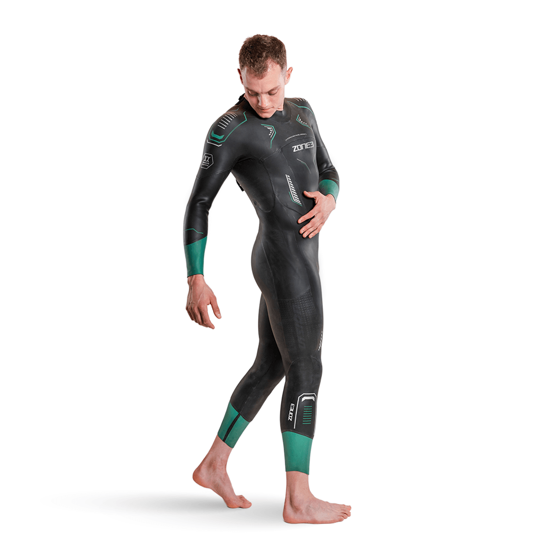 Side view of a man in a black Vision wetsuit with green teal cuffs on sleeves and calves